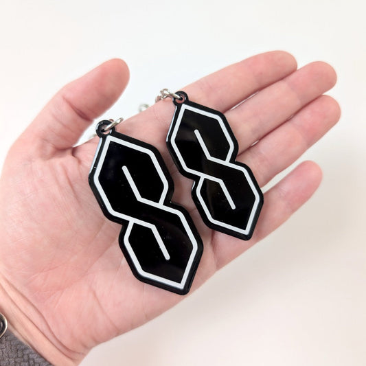 Black and white geometric keychains held in a hand against a neutral background