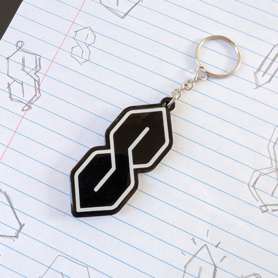 Black geometric keychain on a notebook page with line drawings